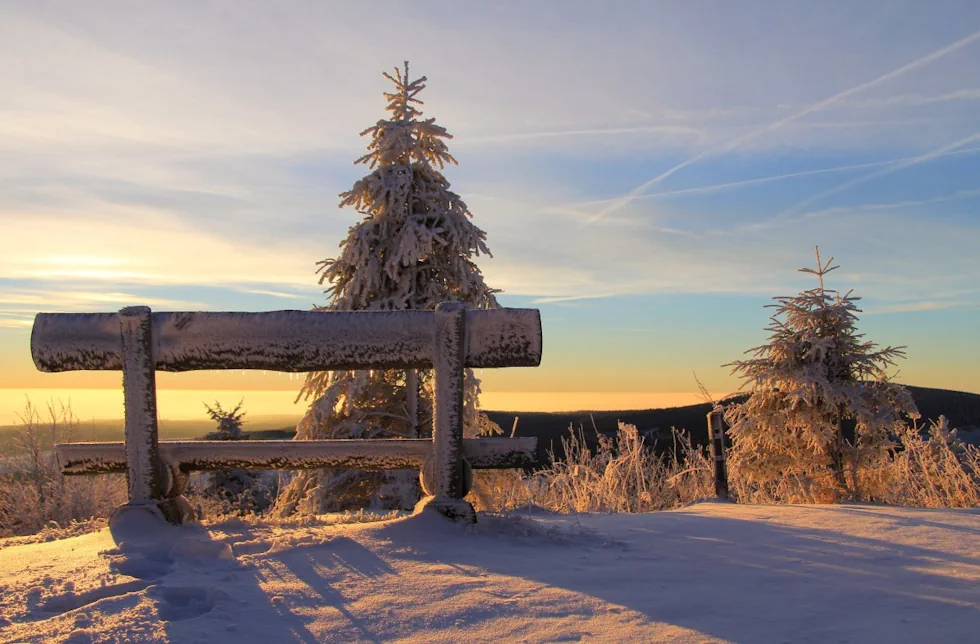 A wooden bench in a snowy landscape looks out upon mountains and sky
