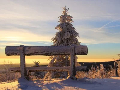A wooden bench in a snowy landscape looks out upon mountains and sky