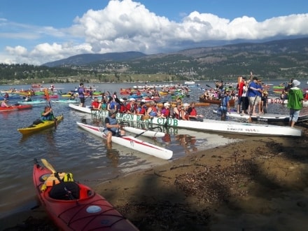 Kayaks and a dragon boat, loaded with people, near the sandy shoreline