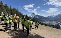 Attendees at the 2025 National Connectivity Conference in Banff stand on a mountain slope overlooking Banff and the mountains beyond it. Photo Credit: A. Michael Bezener