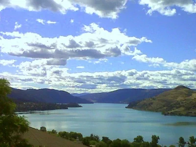 Kalamalka Lake surrounded by hills and mountains and below a cloudy blue sky